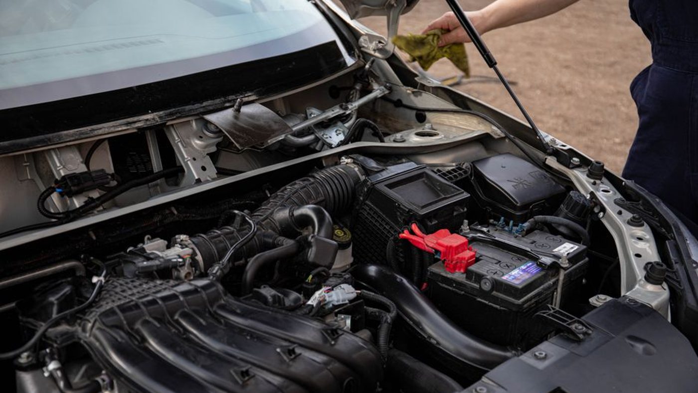 Conducteur qui écoute le bruit d'un moteur capot ouvert dans un garage